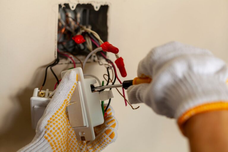 An electrician is replacing a wall switch. A DIY project concept. High voltage danger. installing wire connection using screw driver. The professional wears protective rubber gloves for safety See Less