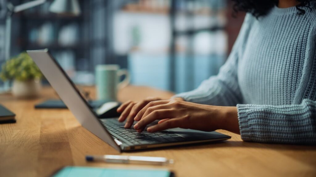 Close Up on Hands of a Female Specialist Working on Laptop Computer at Cozy Home Living Room while Sitting at a Table. Freelancer Woman Chatting Over the Internet on Social Networks. See Less